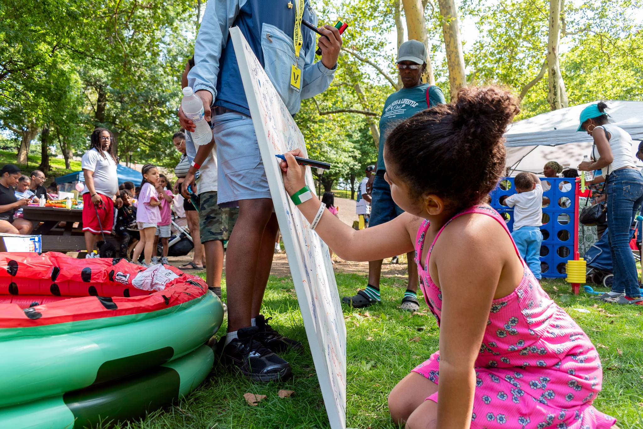 A child signing the large Children’s Day canvas with a volunteer nearby