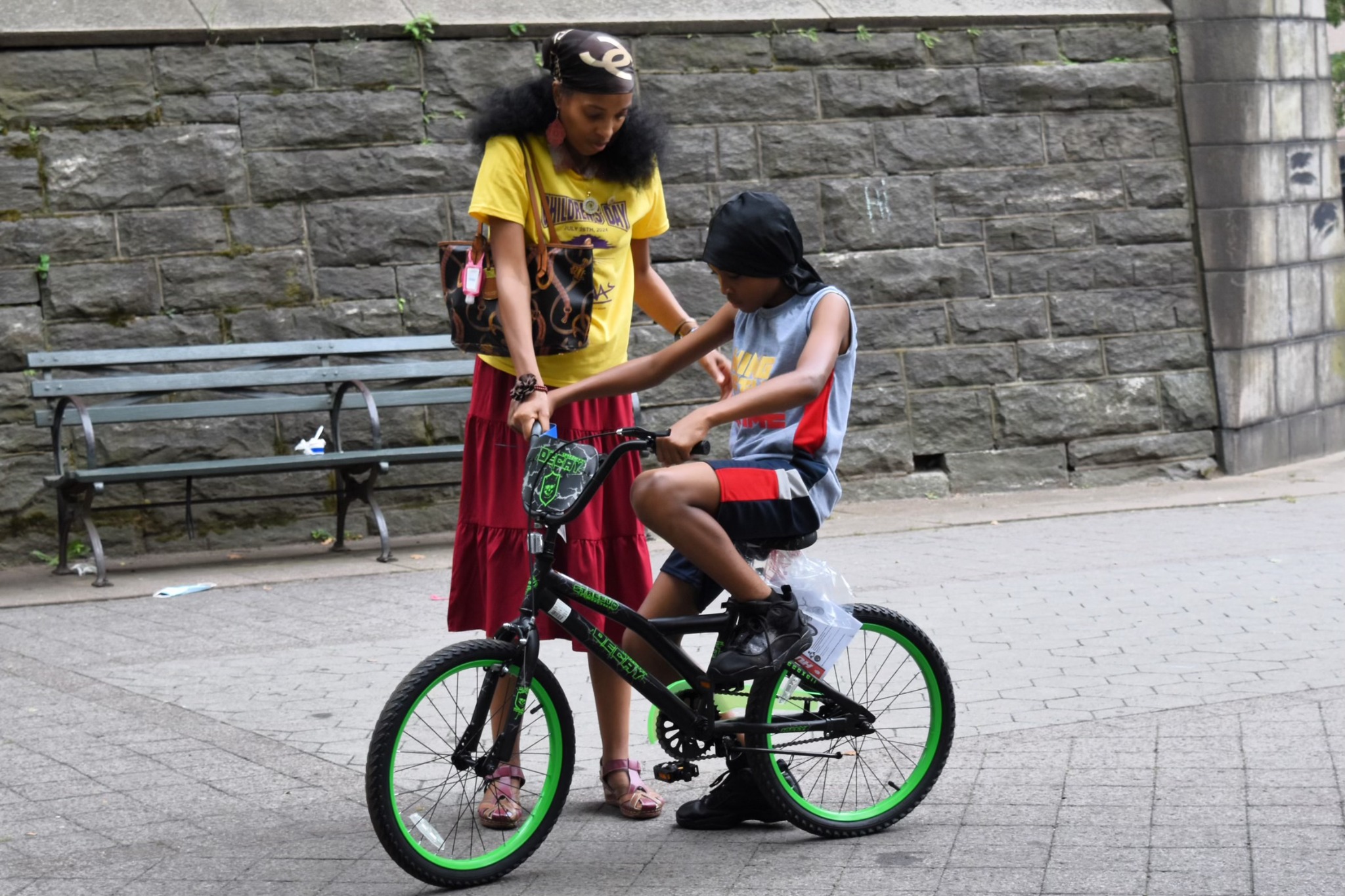 A child being helped while learning to ride a black and green bicycle